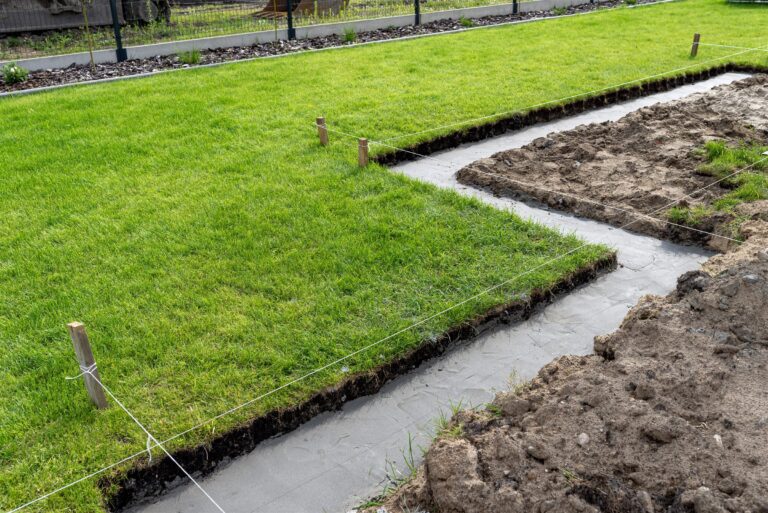 Newly laid lawn marked off with stakes and string beside a work trench