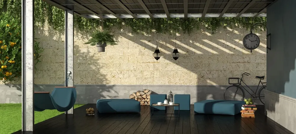 Covered patio with blue outdoor seating under a pergola beside a stone wall