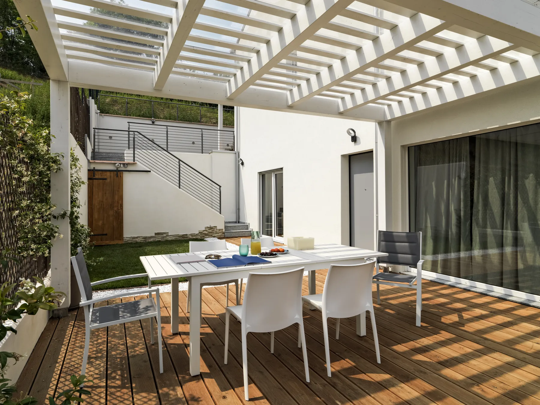Wooden deck shaded by a white pergola over an outdoor dining table and chairs