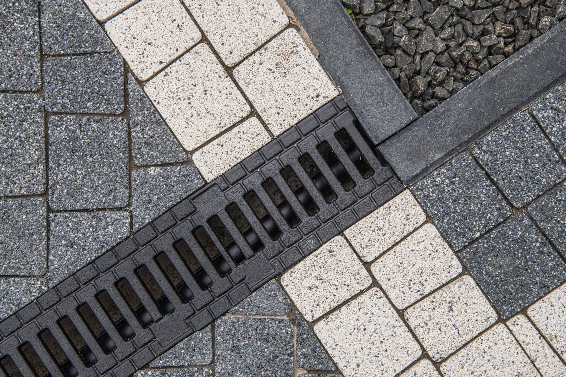 Channel drain with a metal grate running through gray and cream pavers