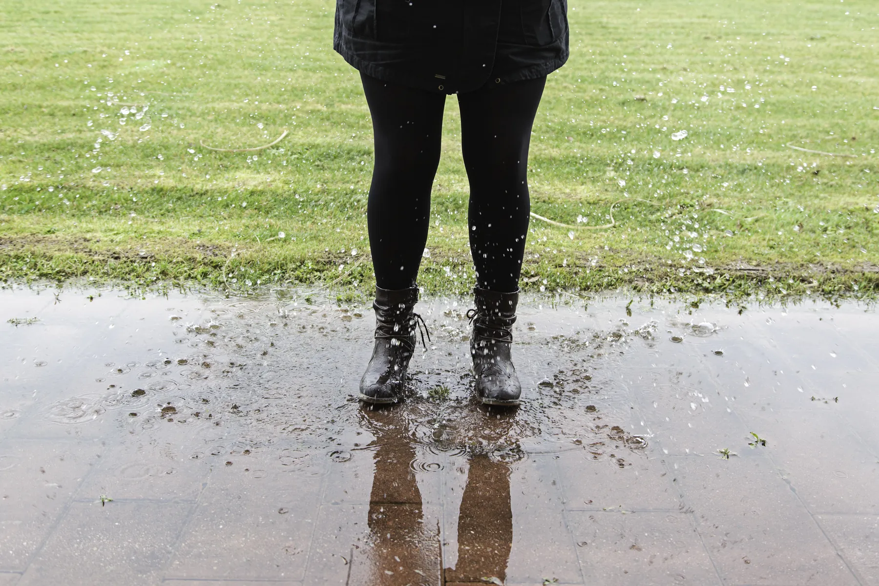 Rain boots standing in a wide puddle of storm water at the edge of a lawn