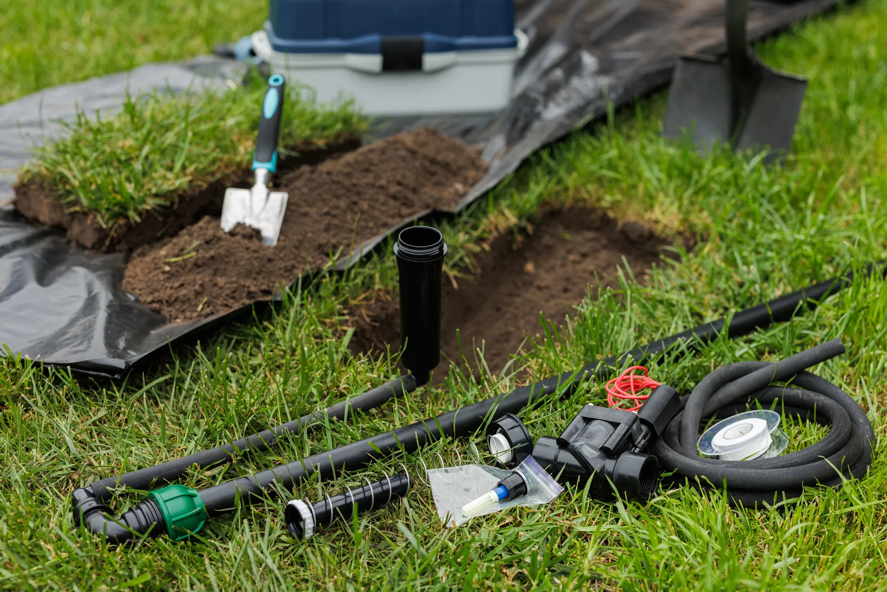 Sprinkler heads, valve box and pipe laid out beside lifted turf for an irrigation install