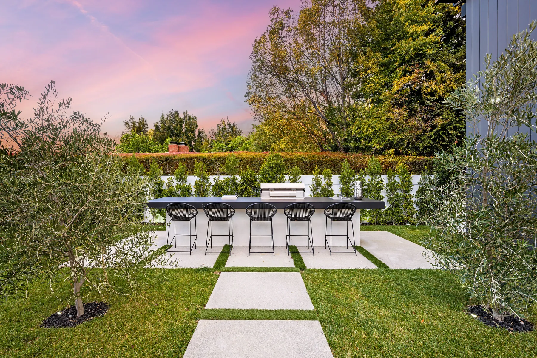 Backyard kitchen island with bar stools at the end of a lawn and stepping-stone path