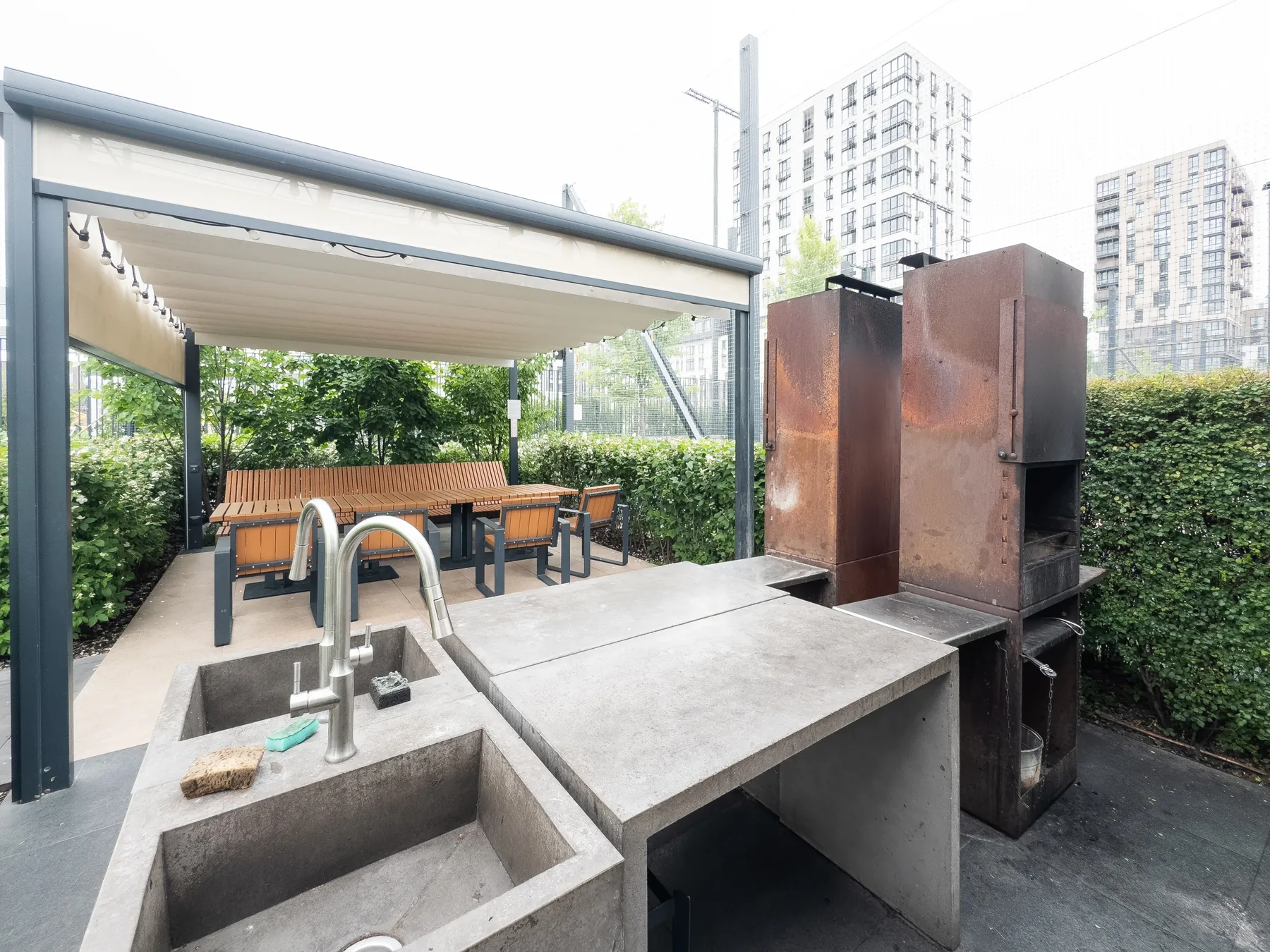 Patio outdoor kitchen with a concrete sink counter, a steel grill and a covered dining table