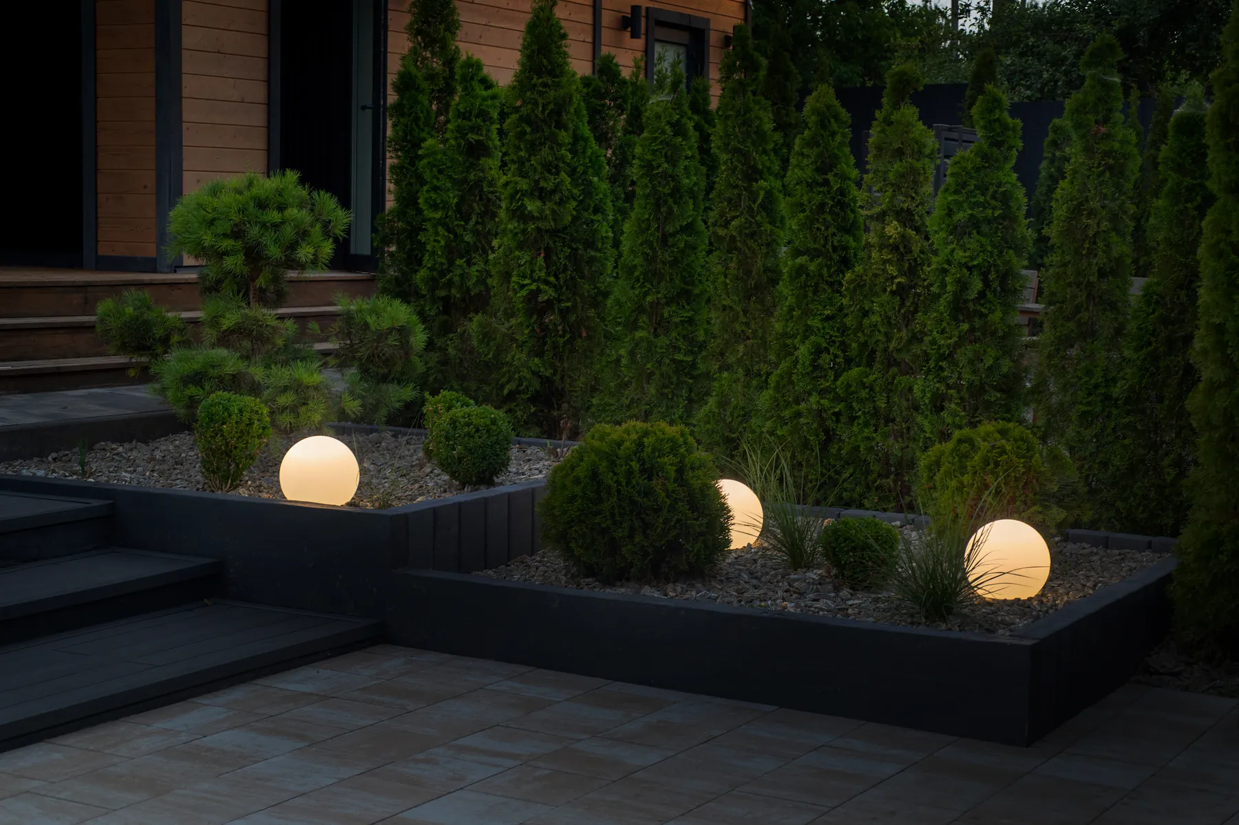 Glowing sphere lights set among clipped shrubs and evergreens in a modern landscape at dusk
