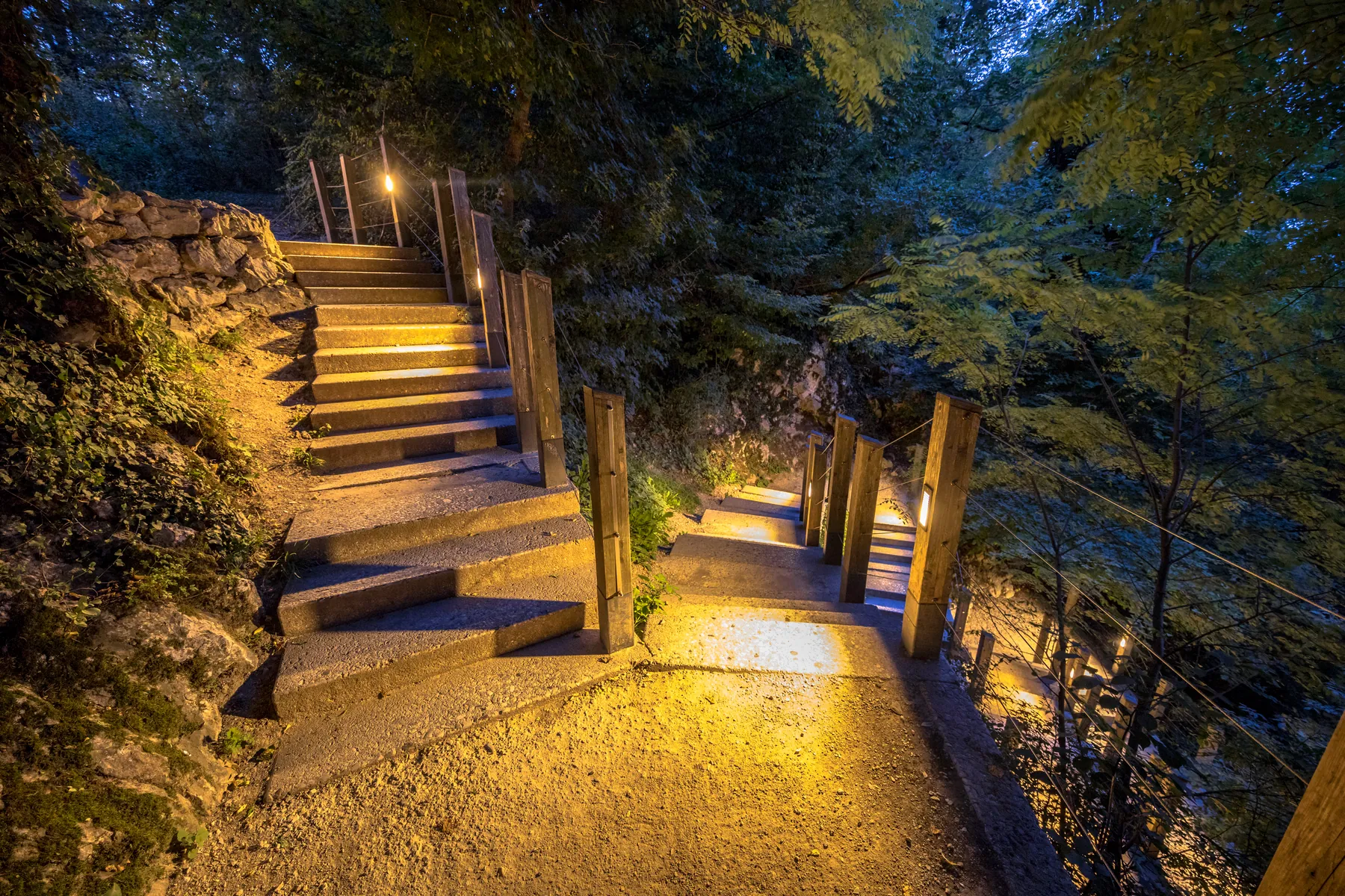 Outdoor stone steps lit by low lights along a wooden railing at dusk