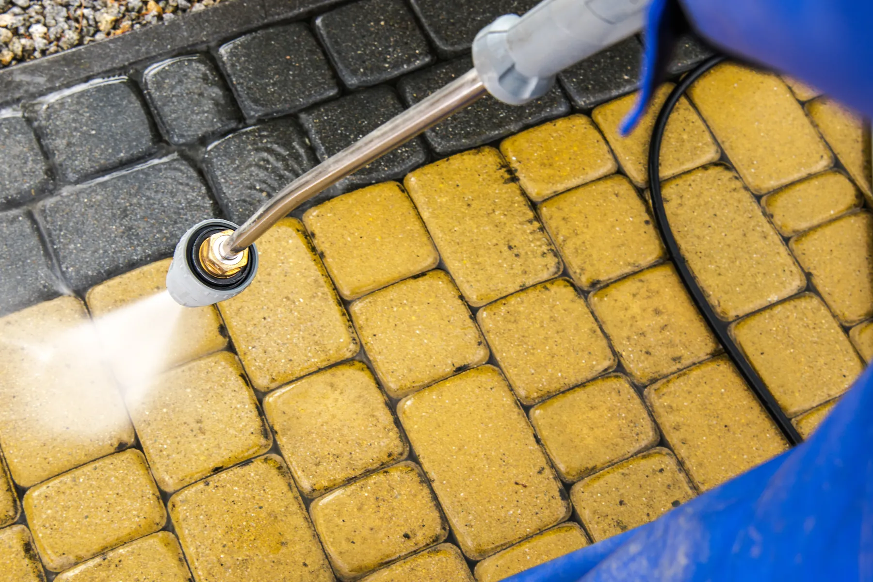 Close-up of a pressure washer nozzle cleaning yellow and gray pavers