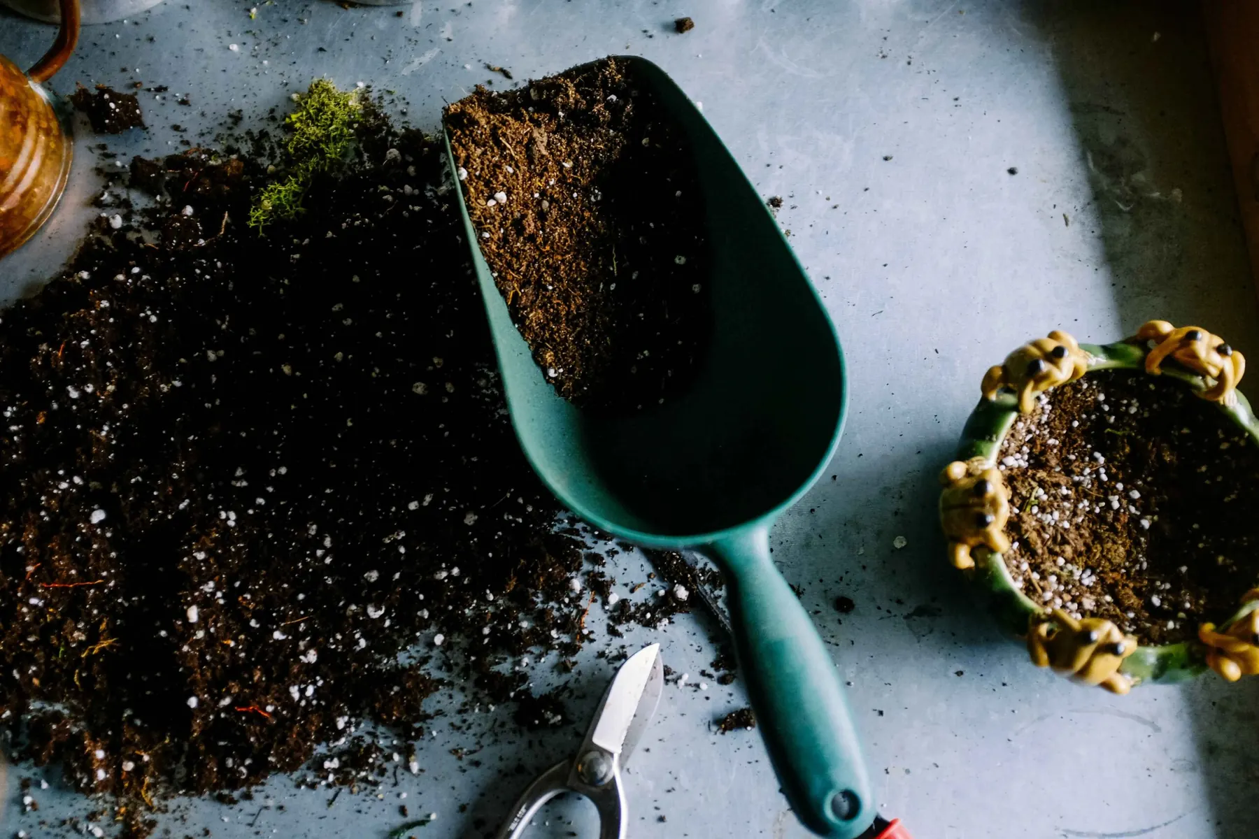 Garden trowel full of potting soil beside a small pot and pruning shears on a table