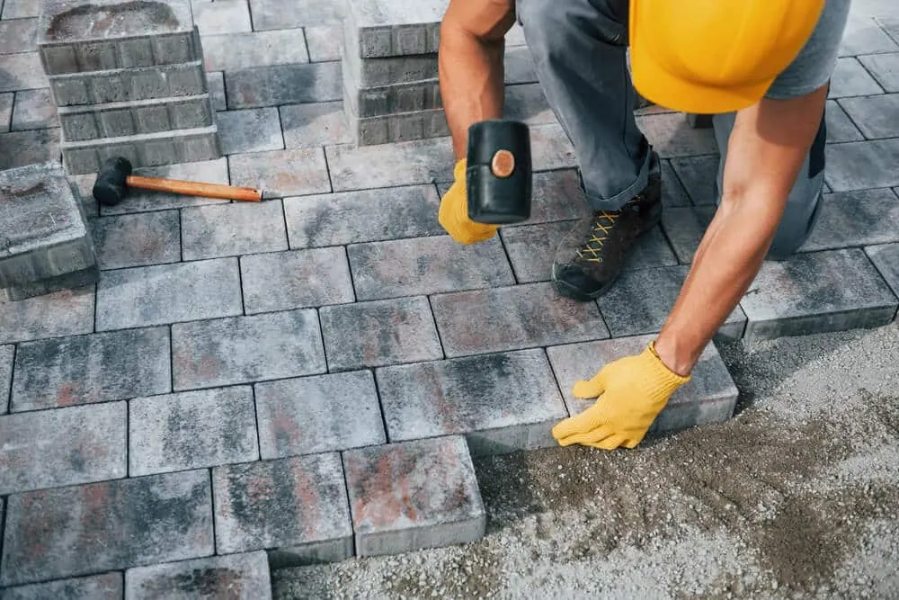 Worker setting grey paving stones with a rubber mallet
